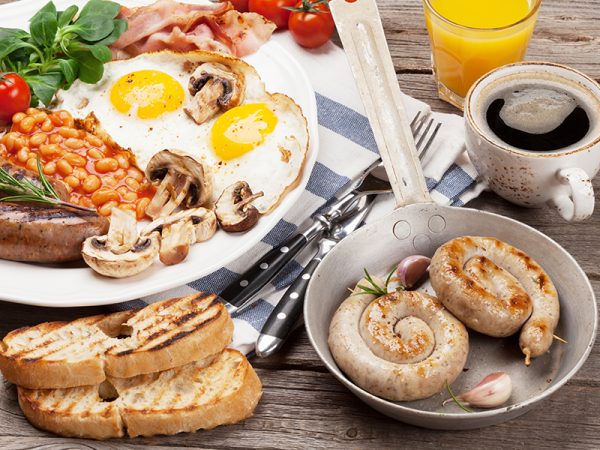 English breakfast. Fried eggs, sausages, bacon, beans, toasts, tomatoes, orange juice and coffee cup on wooden table